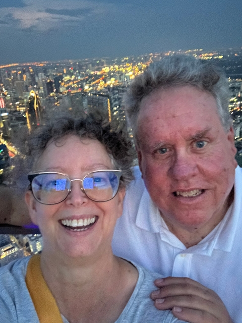 Close-up of two smiling people with city lights in the background.