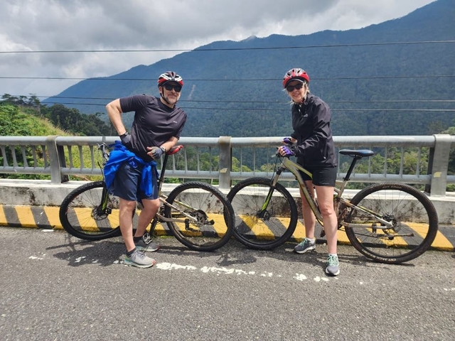       Two cyclists posing with their bikes on a bridge with mountains.
  