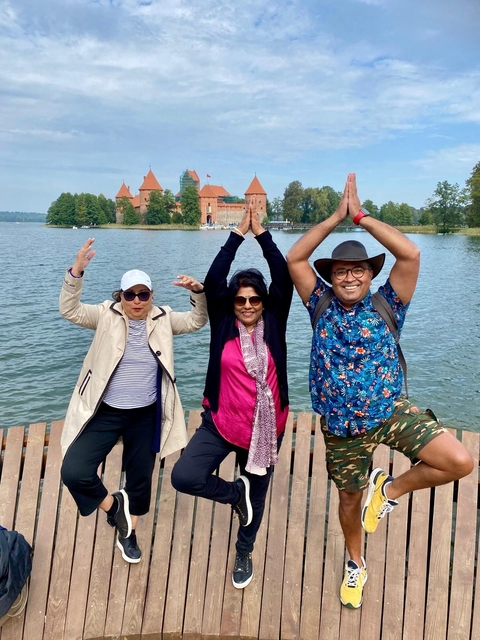 Three people posing with hands raised in front of a red building by a lake.