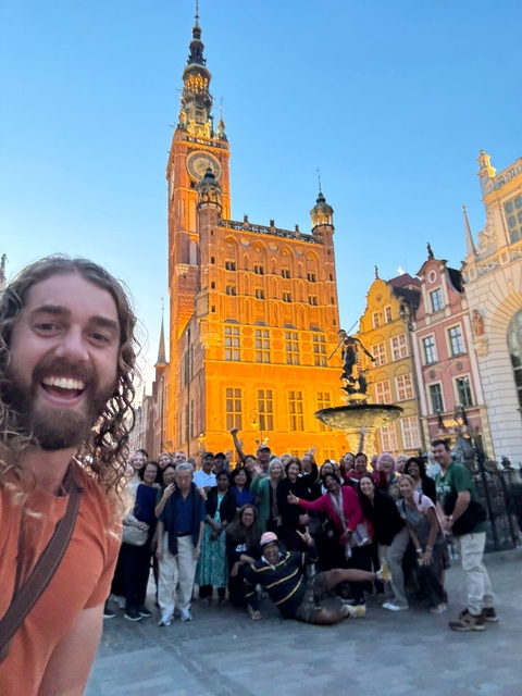 A group of people posed in front of a red building with a fountain.