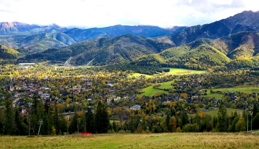 Panoramic view of a town surrounded by mountains in autumn.