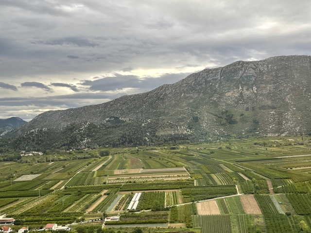 Expansive fields and mountains under a cloudy sky.