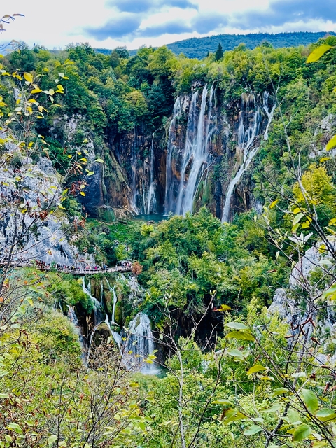       Waterfall cascading down cliffs into lush greenery.
  