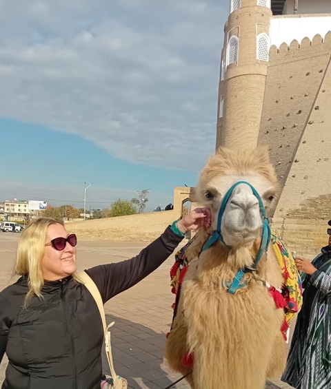       Woman petting a camel with historical architecture in the background.
  