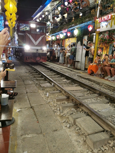Tourists near train tracks as a train approaches.