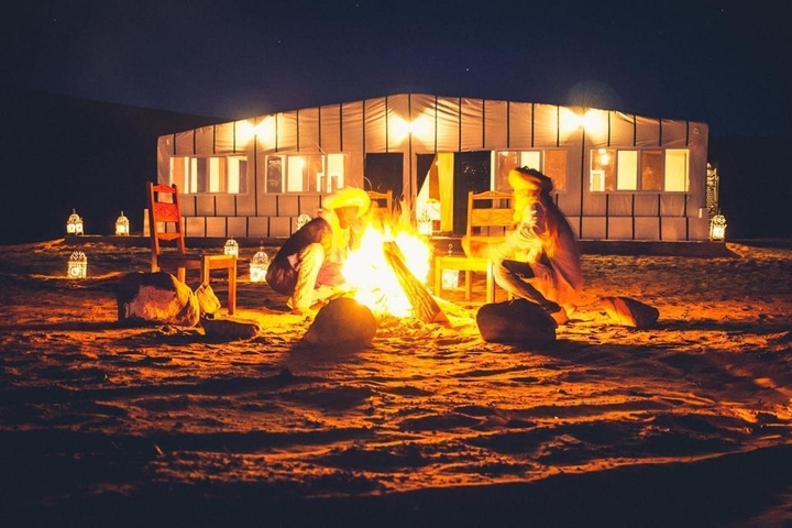 Two people sitting by a fire in front of a tent at night.