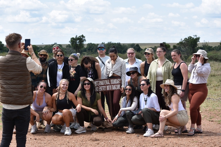       Group posing near a sign on a grassy plain.
  