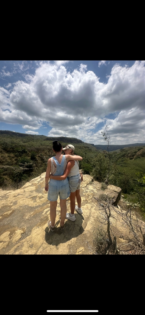       Two people embracing while overlooking a lush landscape.
  