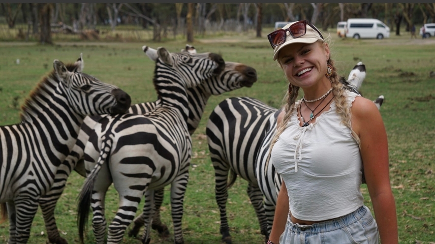      Tourist posing with a group of zebras in a grassy field.
  