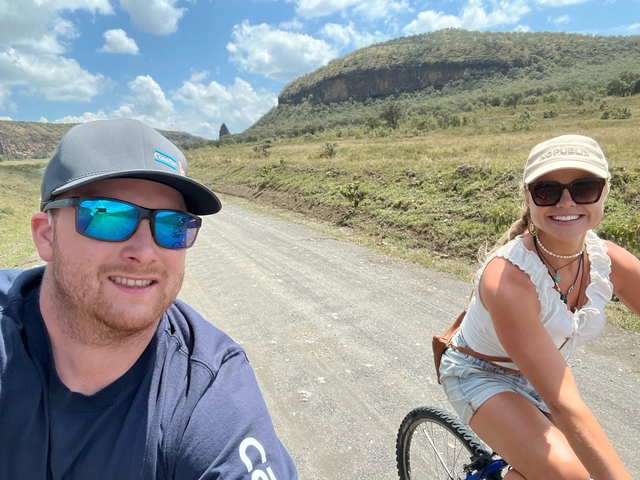       Two people biking on a path with a landscape view.
  