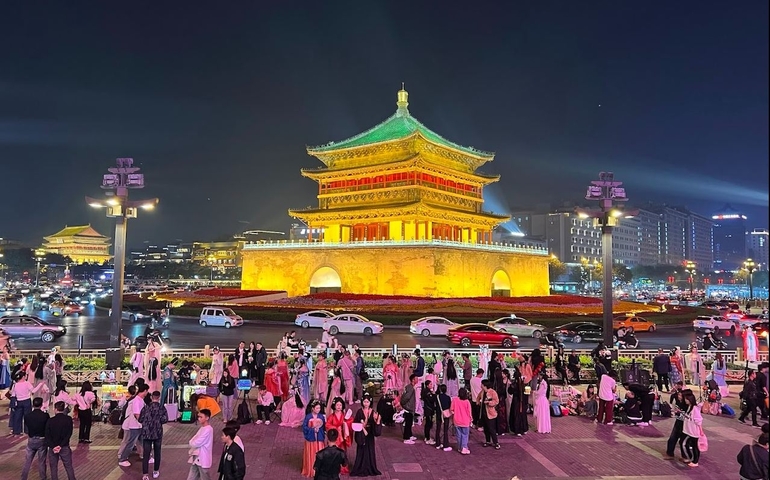 Illuminated traditional building surrounded by crowds at night.
