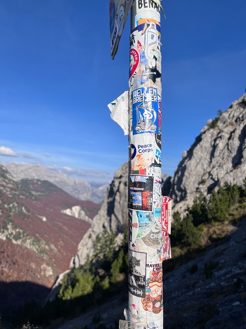 A signpost covered in stickers with mountains in the background.