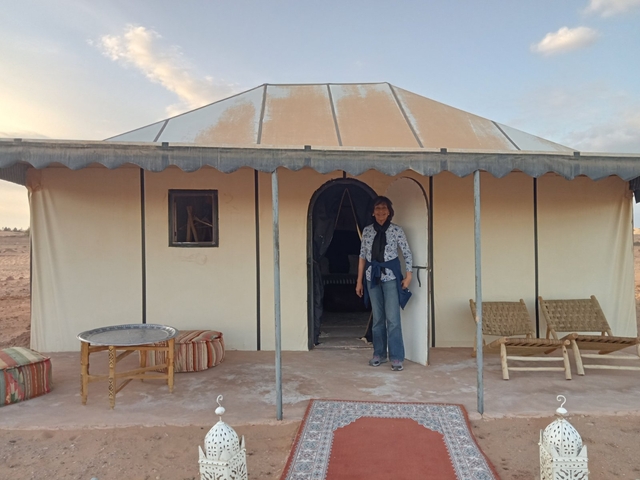       A person standing in front of a tent in a desert area.
  