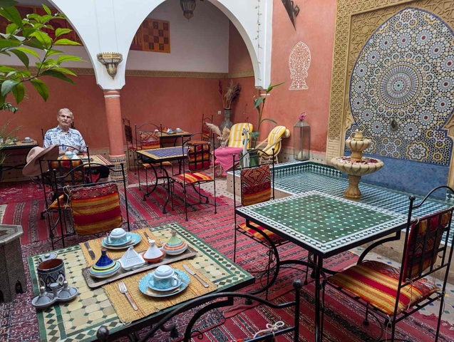       A courtyard with colorful tiles, tables, and a person sitting.
  