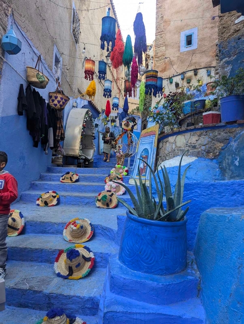       A colorful, blue-painted street with hats and souvenirs.
  