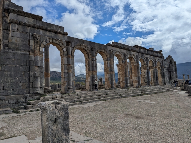       Roman ruins with arches and tourists.
  