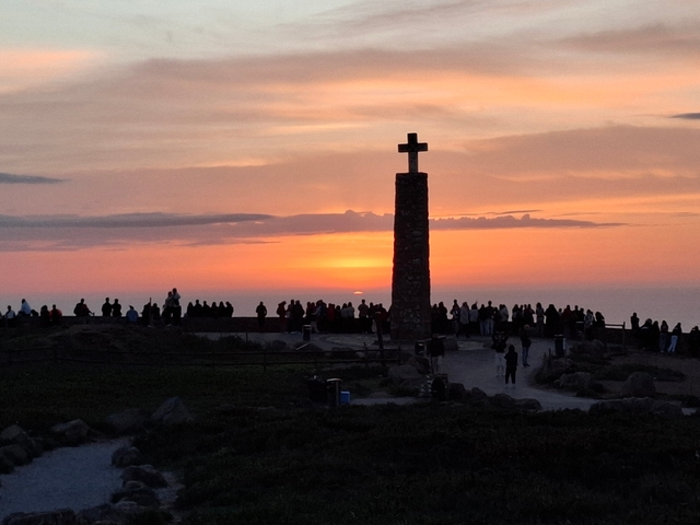 A crowd watching the sunset at a monument with a cross.