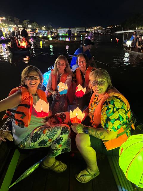 Women on a boat at night, holding illuminated paper lanterns.