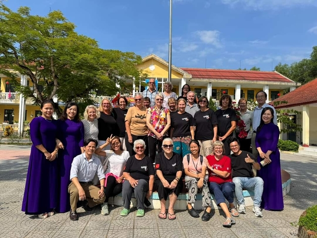 Large group of people posing in front of a yellow building