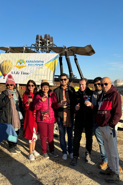       Group of people holding drinks with a hot air balloon basket in the background.
  