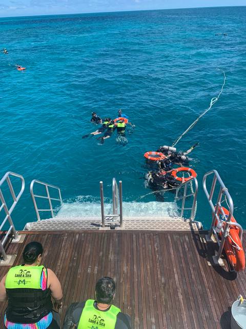 Scuba divers swimming in clear blue water next to a boat.