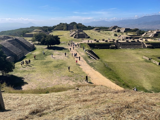       Wide view of ancient ruins with tourists walking around.
  