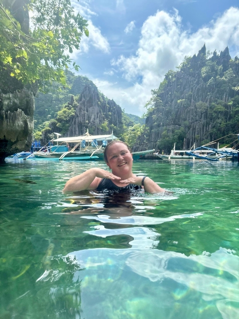 A woman in the water with a scenic backdrop of limestone cliffs and boats.