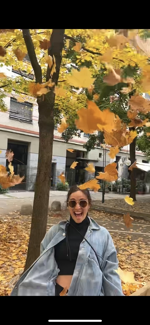 Person throwing leaves in the air amidst urban buildings.