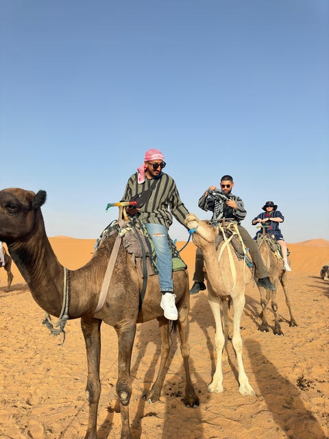Group of people riding camels in a desert landscape.