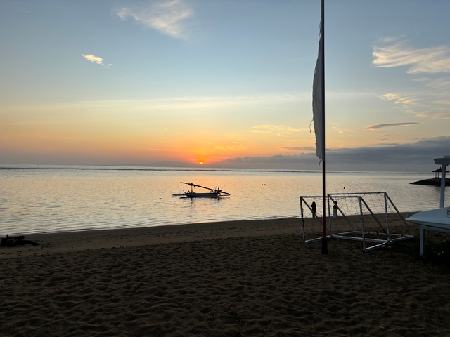 Sunset view of a beach with a small boat in the water.