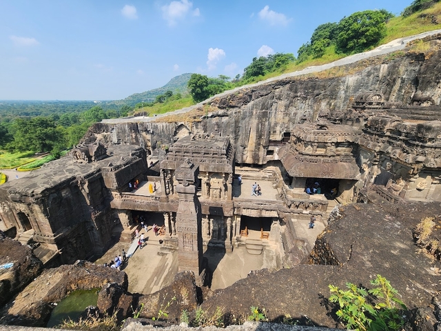       People exploring large ancient stone structures carved into the hillside.
  