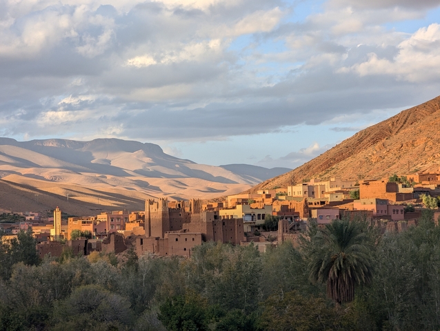 Sunlit view of an adobe Moroccan village with mountains in the background.