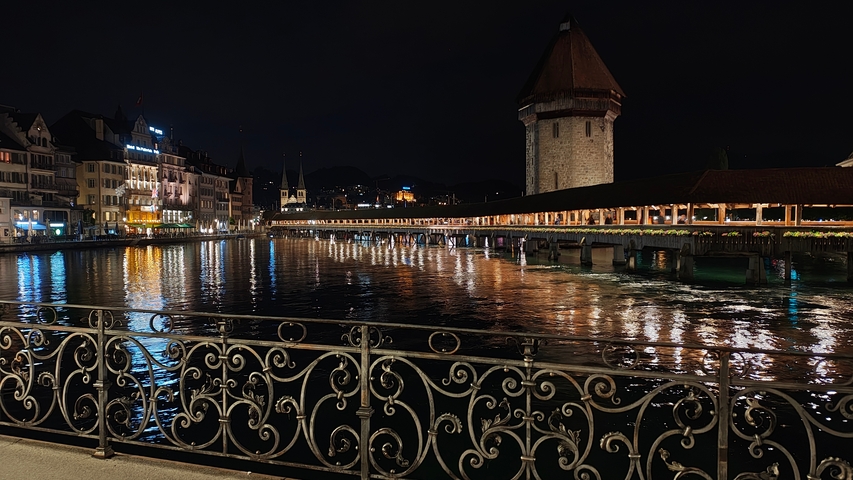 Night view of Chapel Bridge in Lucerne with reflections on water.