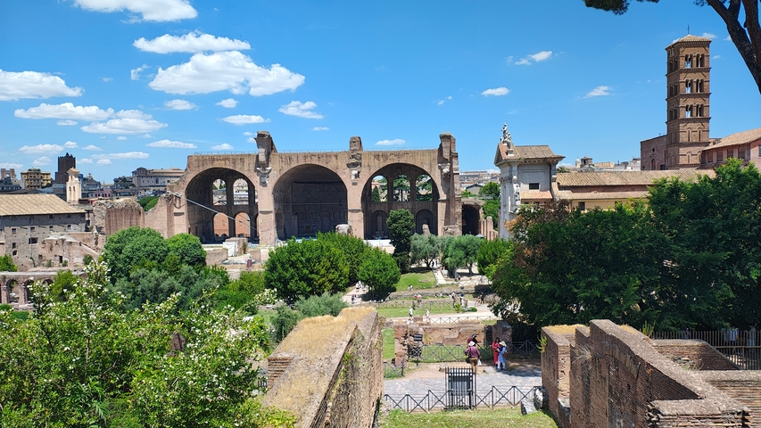       Ancient ruins with tourists exploring under a blue sky.
  