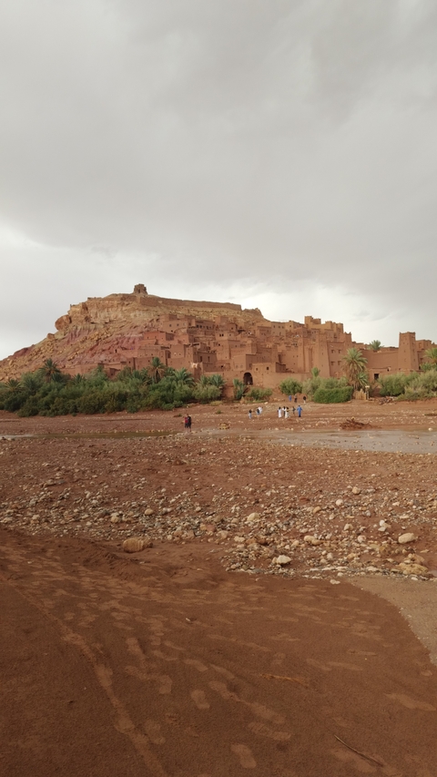 Ancient kasbah with people in the foreground on a rocky terrain.