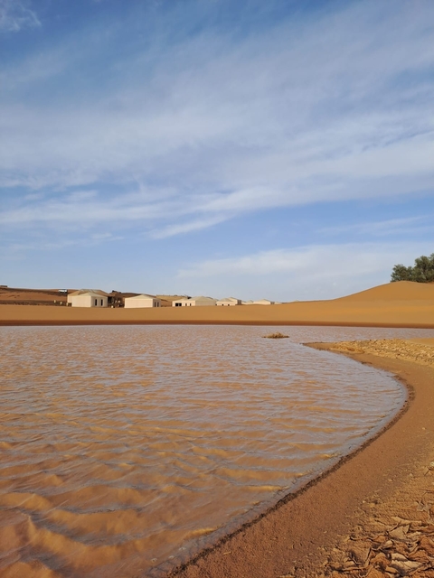 Small settlement with huts near dunes and a body of water.