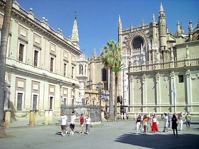 People walking near the Seville Cathedral with palm trees.