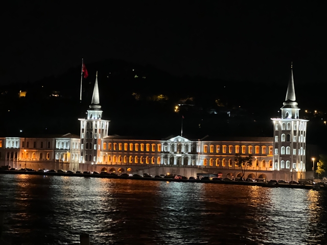       Building with spires illuminated at night across the water.
  