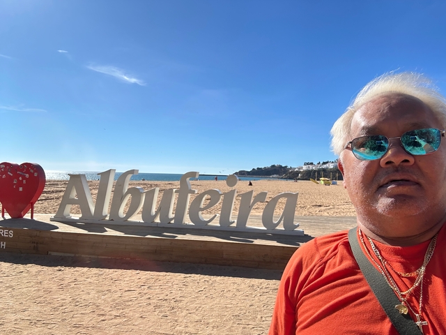 Person near a beach sign with Albufeira in the background.