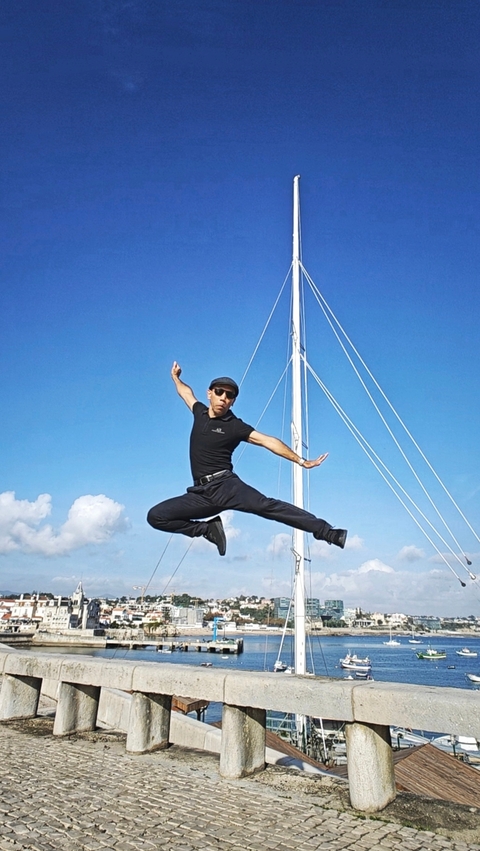 Person jumping with a sailboat mast in the background.