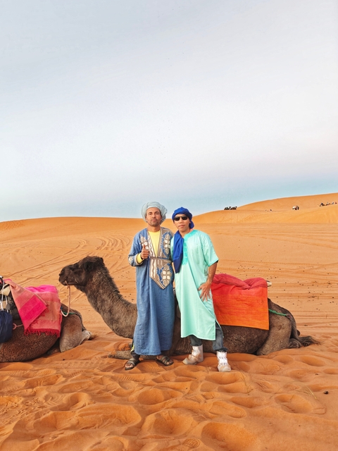 Two people standing with camels in a desert.