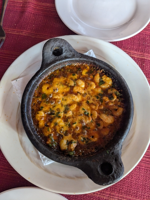 A dish of sizzling shrimp in a dark sauce served in a rustic pot.