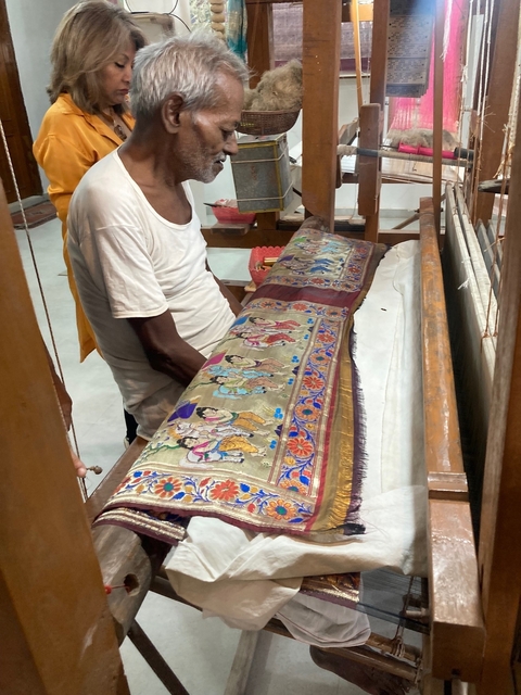       Person working on a traditional loom with an intricate design.
  