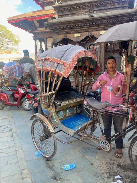       Man standing next to a traditional cycle rickshaw.
  