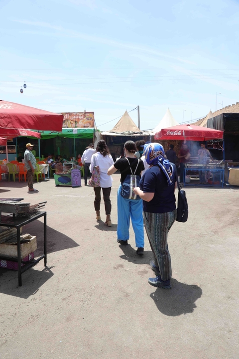       People walking in a busy outdoor market with colorful stalls.
  