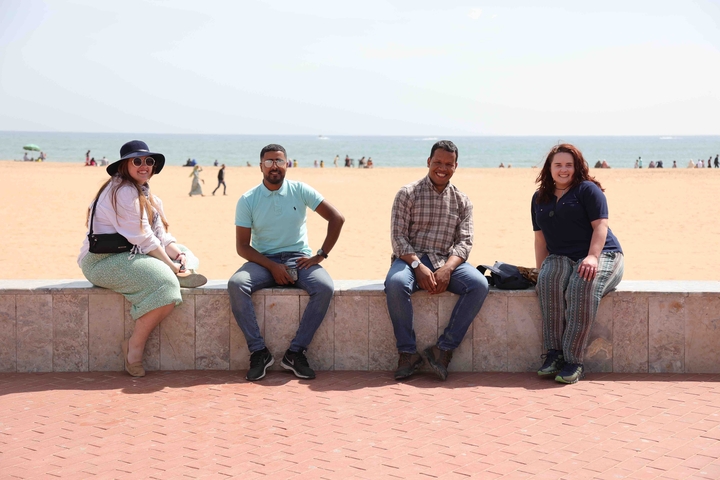       Four friends sitting on a ledge with beach in the background.
  