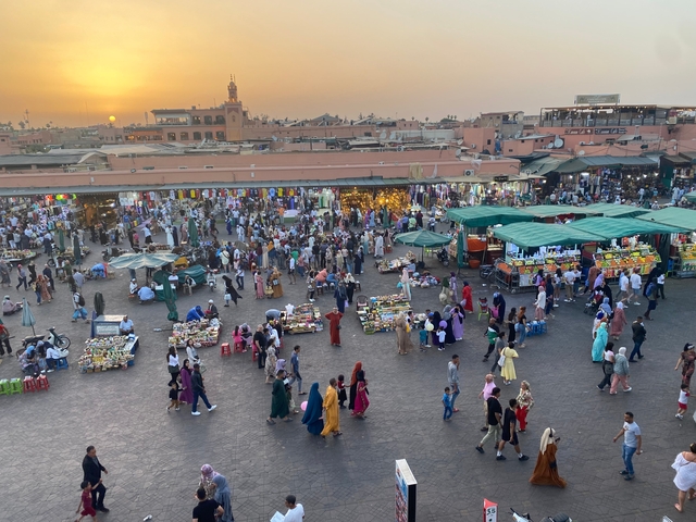       Busy market square at sunset with people and stalls.
  