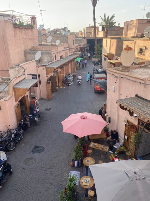      View of a bustling market street from above with a pink umbrella, people and stalls.
  