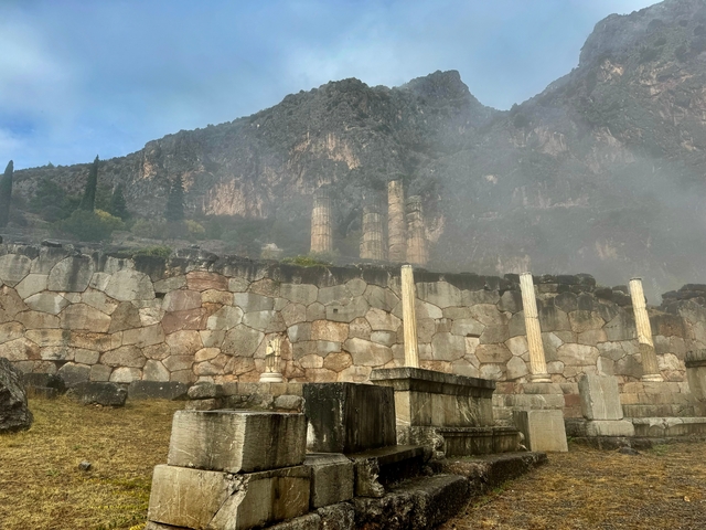 Ancient ruins with columns under a cloudy mountain.