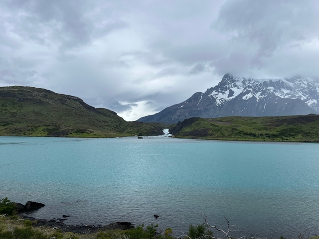 Turquoise lake surrounded by hills with snowy mountains in the distance.